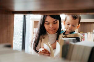 Young mother reading books to little son in library.