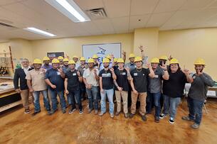 A group of students wearing yellow hard hats smile for a photo