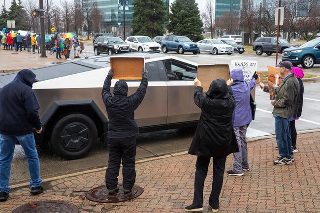 People protest against Tesla as a Cybertruck drives by.