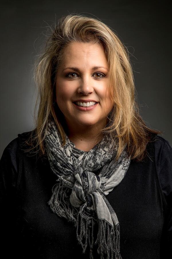 Colleen Sorensen smiles for a headshot wearing a black sweater and a gray fashion scarf.