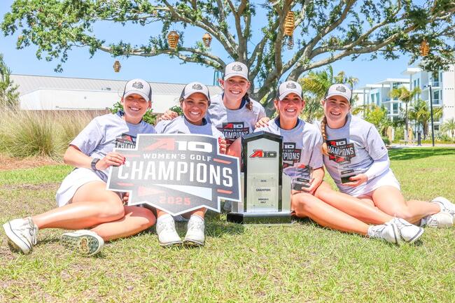 Five women pose outside with a golf championship trophy