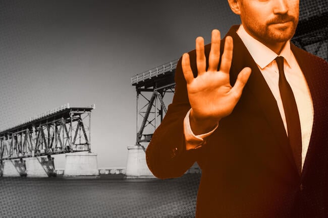 A person in a suit holding their hand up in a stop gesture with a broken bridge in the background.