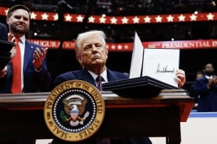 President Donald Trump holds up a signed piece of paper while sitting at a desk inside Capital One Arena
