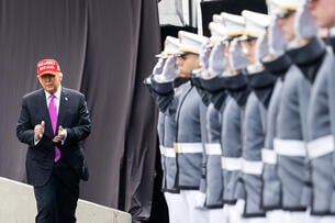 Donald Trump, wearing a red Make America Great Again hat that clashes with his fuchsia tie, walks past a line of saluting, gray-uniformed West Point cadets.