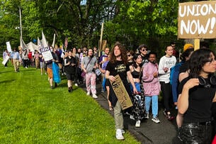 People march outside, some carrying signs, one of which says, "Union Now!"