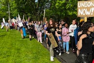 People march outside, some carrying signs, one of which says, "Union Now!"