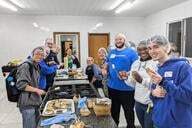 A group of young people work preparing meals wearing blue sweatshirts and hairnets