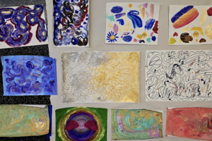 A photo of a dozen paintings on a white background, each painting has abstract shapes and figures. 
